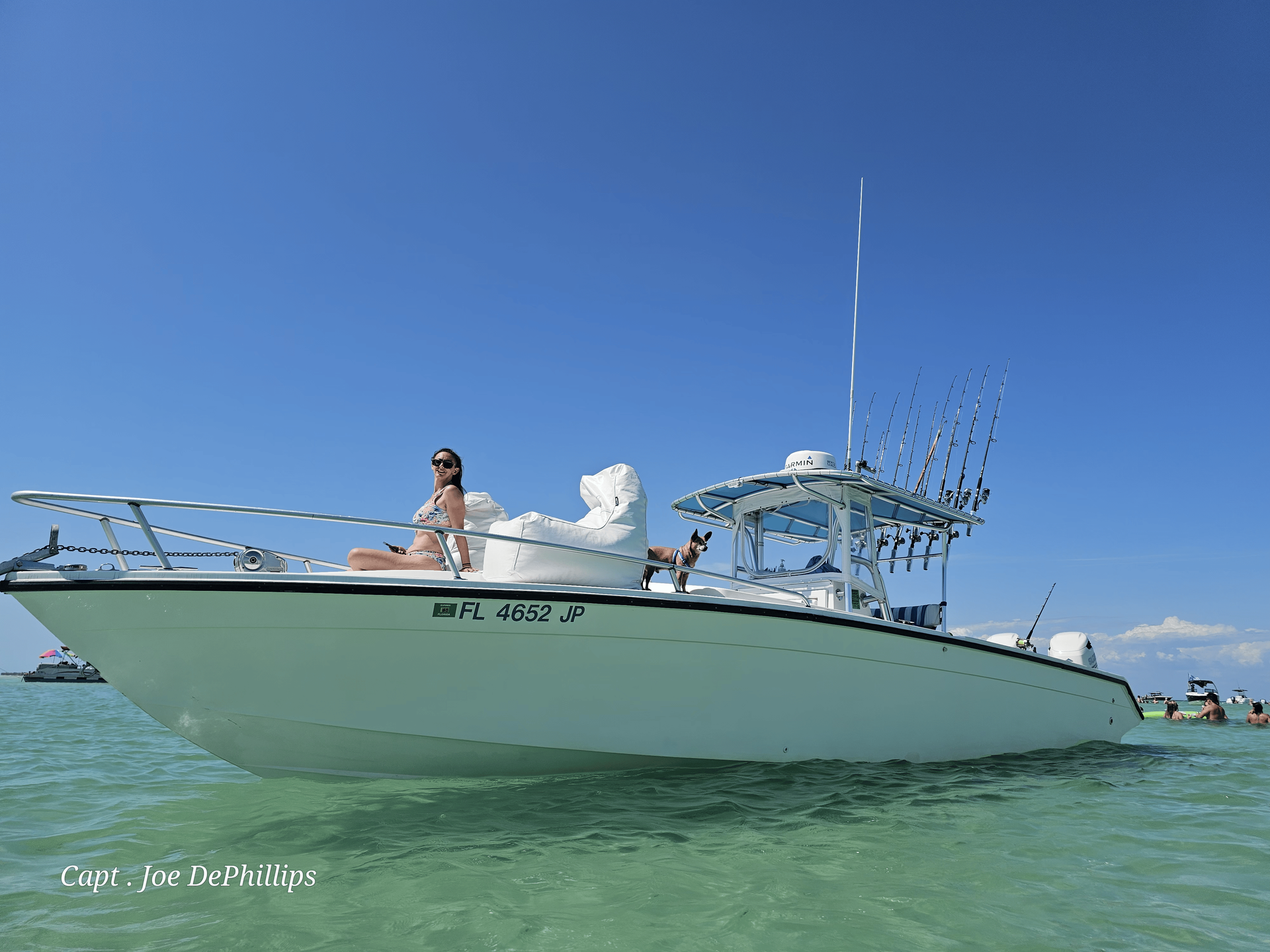 White boat in shallow turquoise water with a woman sunbathing on the bow under a clear blue sky.