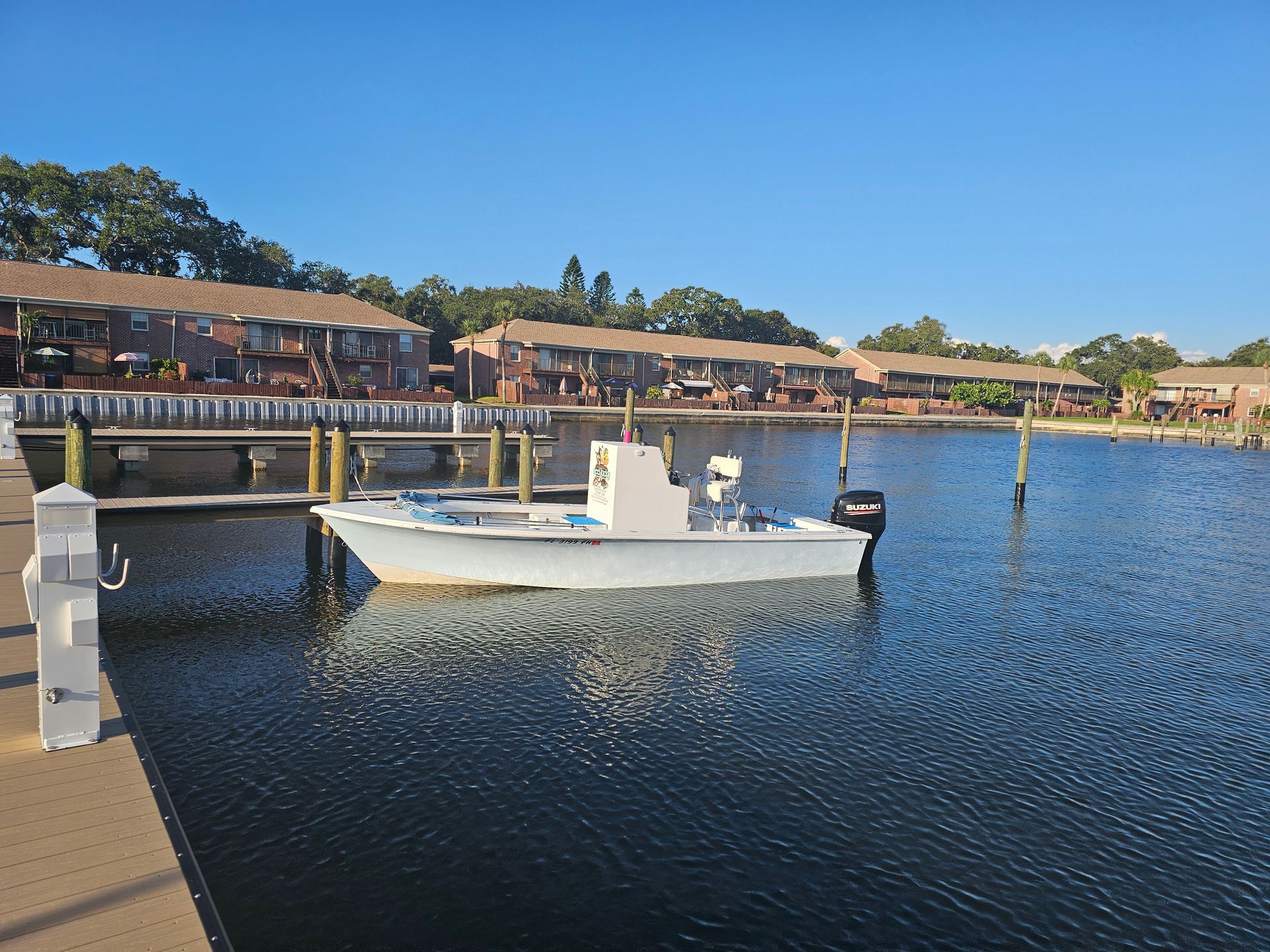 A small white boat docked on a calm body of water in front of apartment buildings.