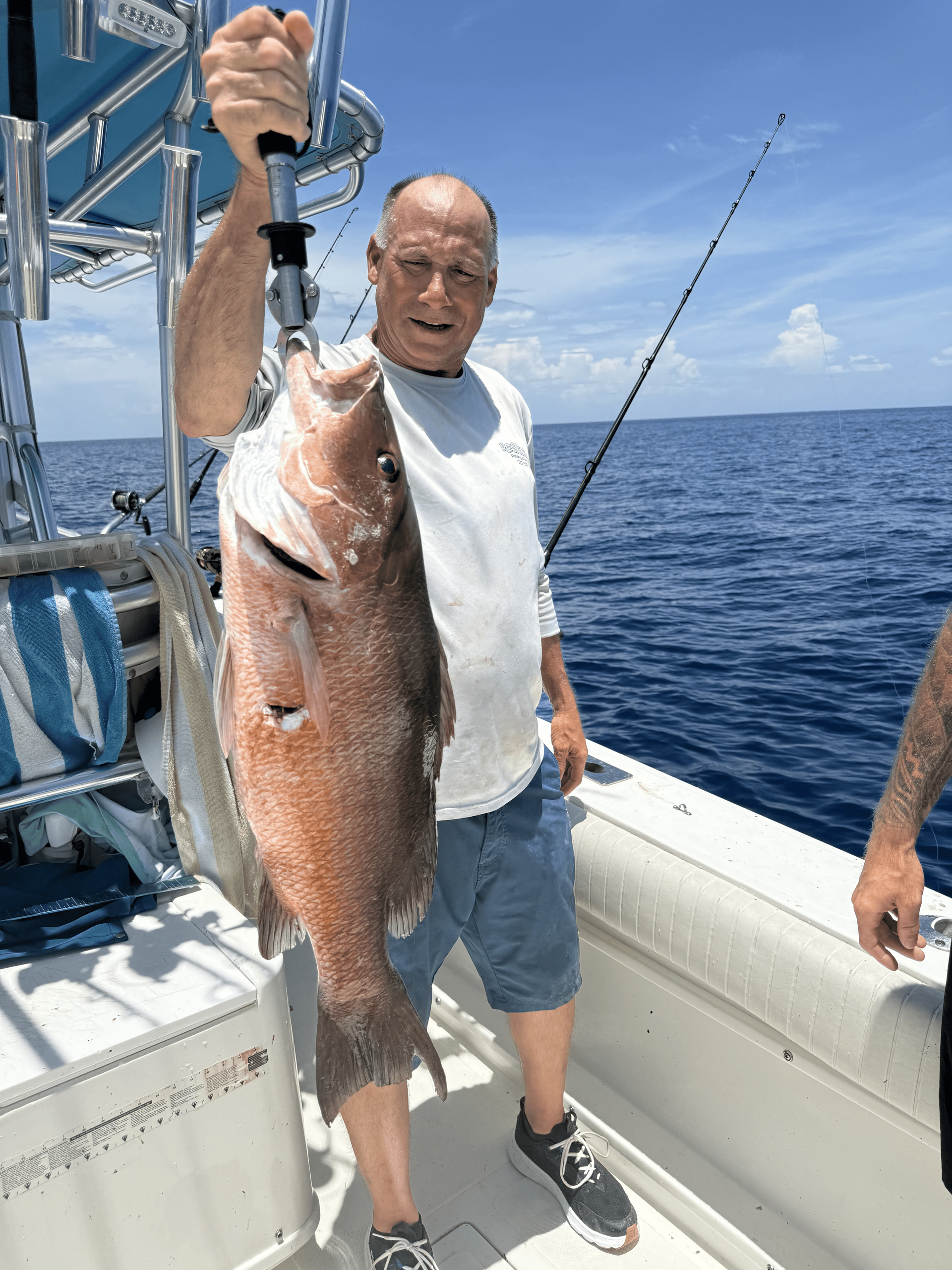 Man on boat holding a large red snapper. Sunny day, ocean background.