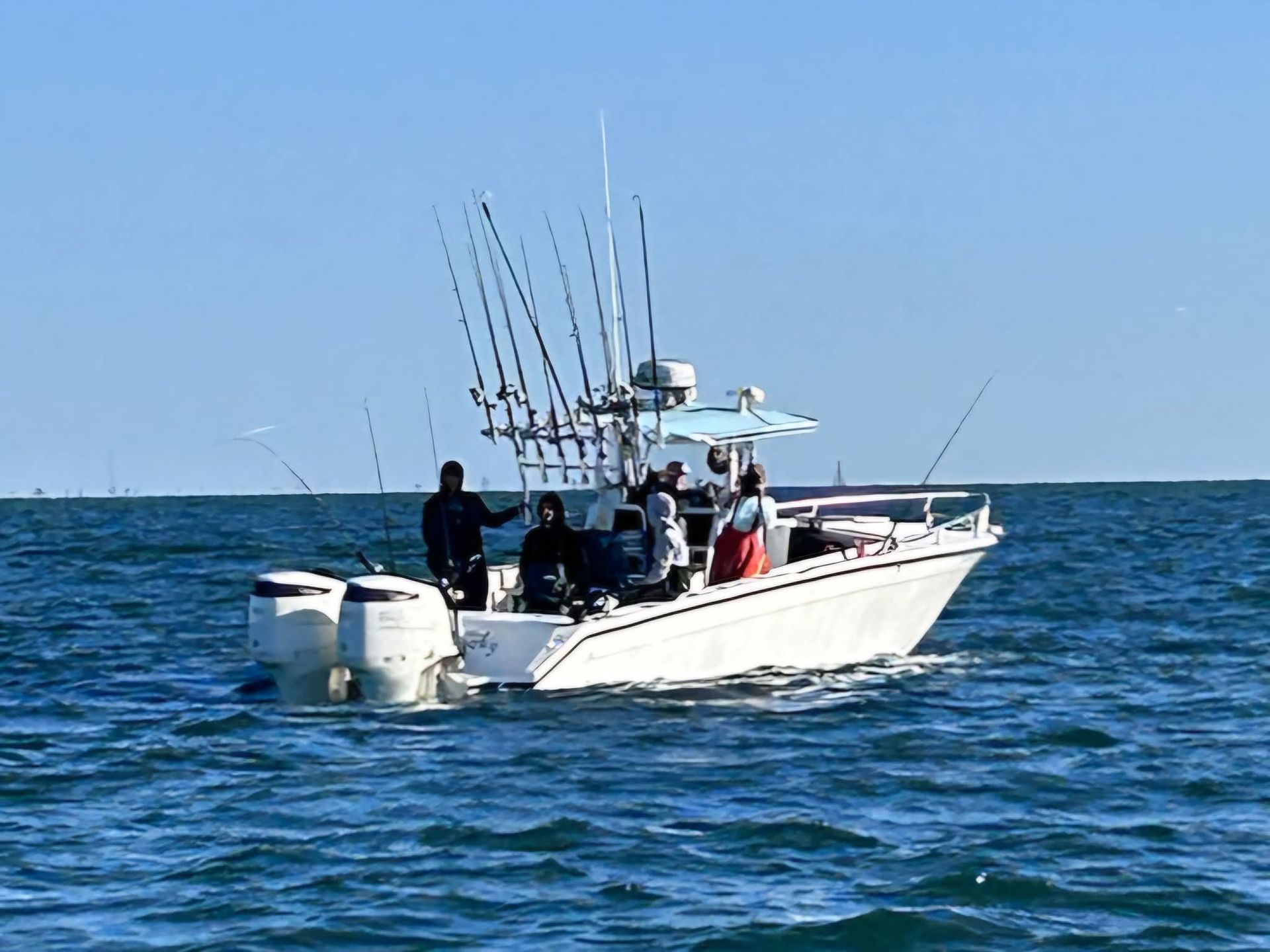 Fishing boat on the water with multiple rods; people aboard. Blue sky, sunny day.