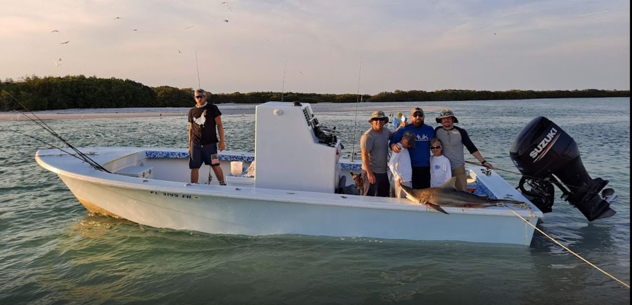 People on a boat with a large fish, in the water, possibly fishing.