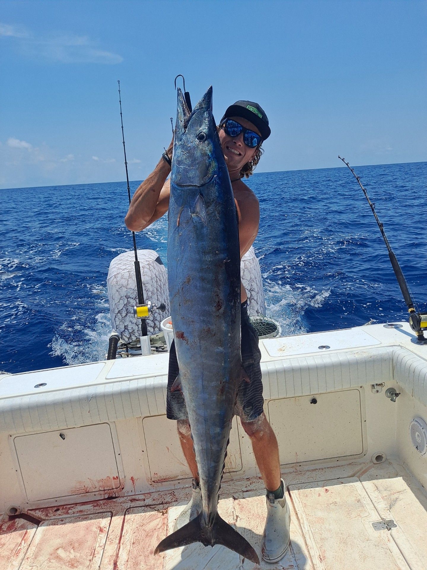 Man holding a large, blue fish on a boat at sea, smiling.