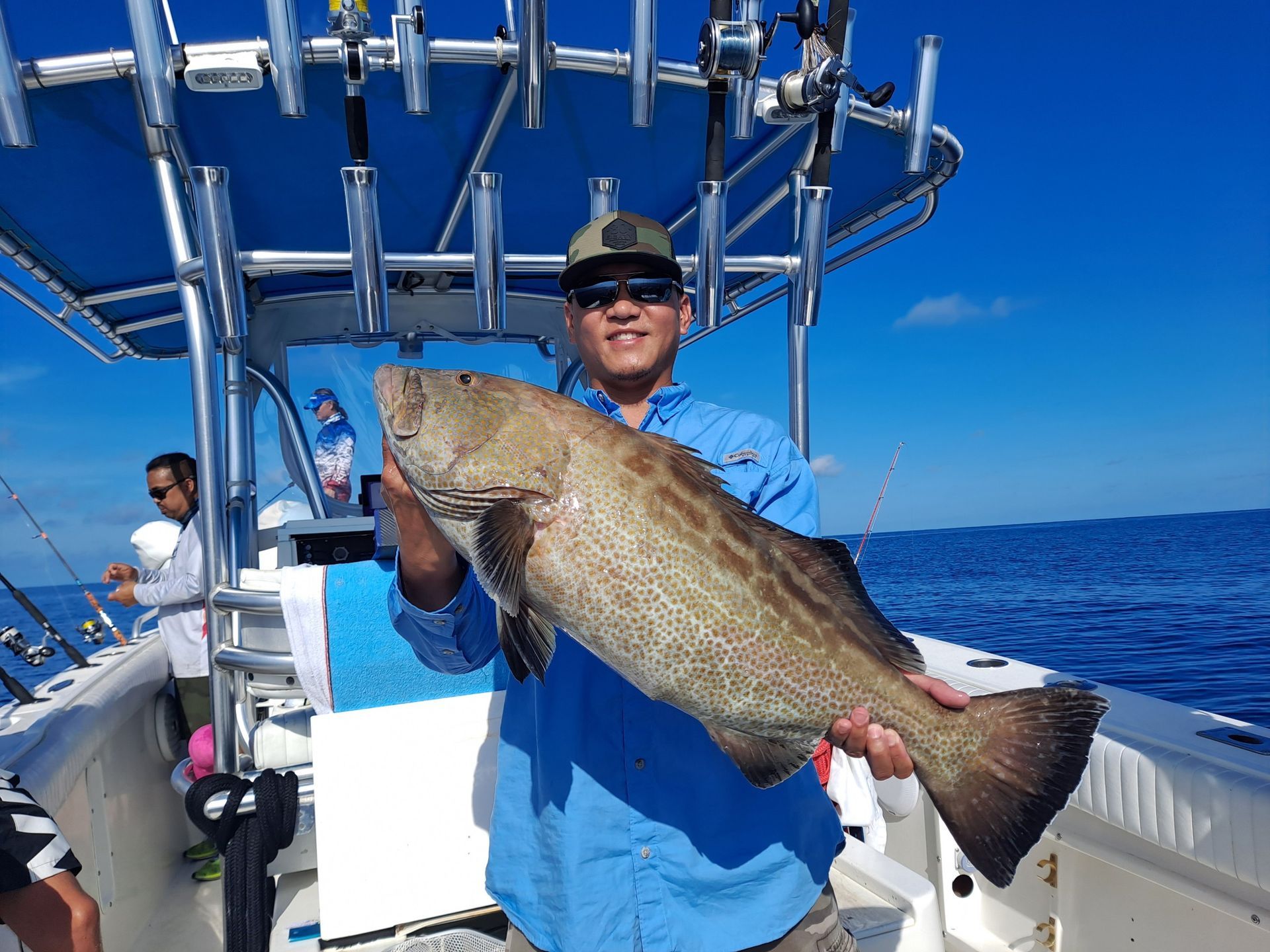 Man holding a large fish on a boat under a blue sky.