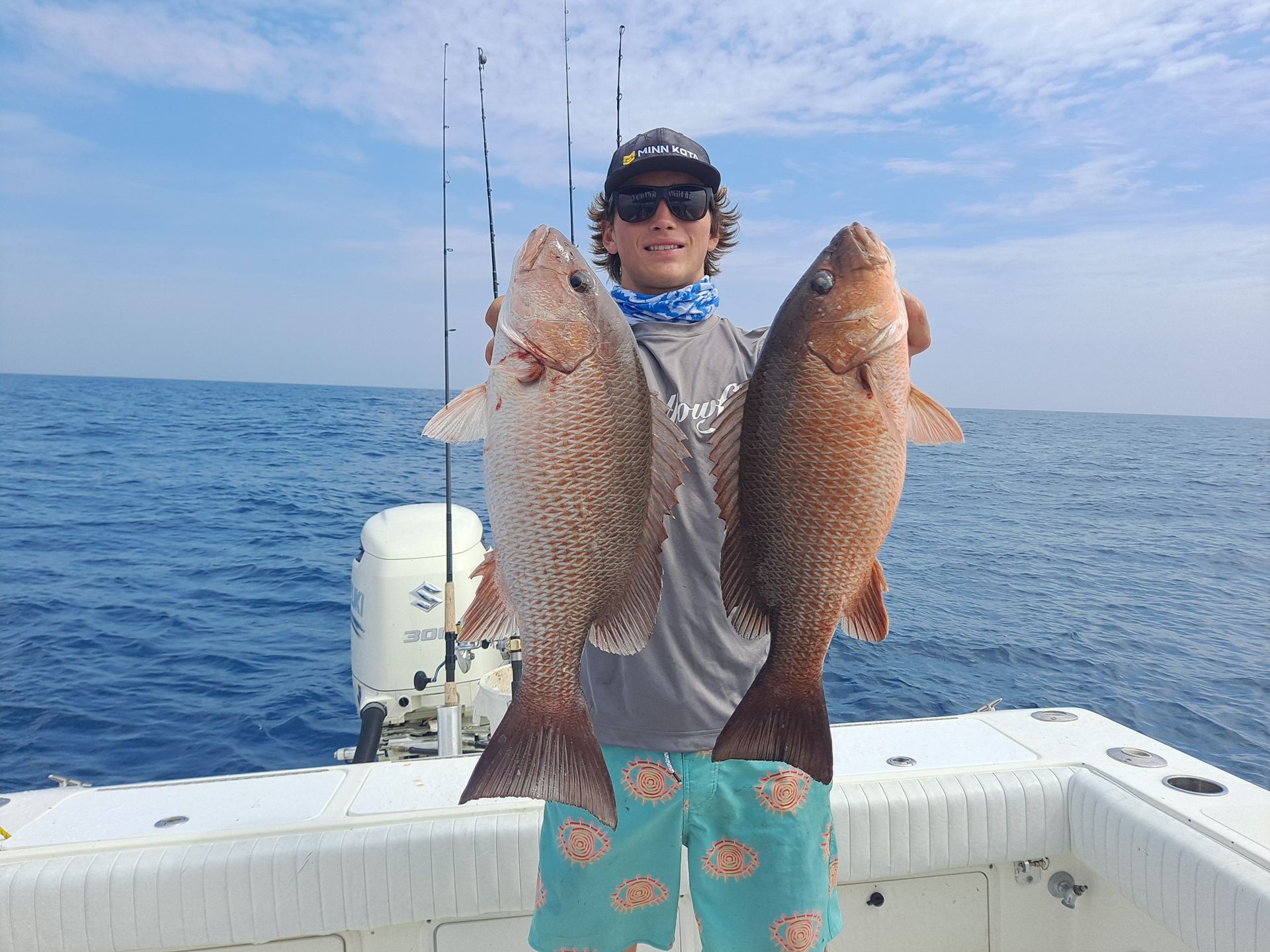 Man on boat holding two large red snapper fish, ocean background.