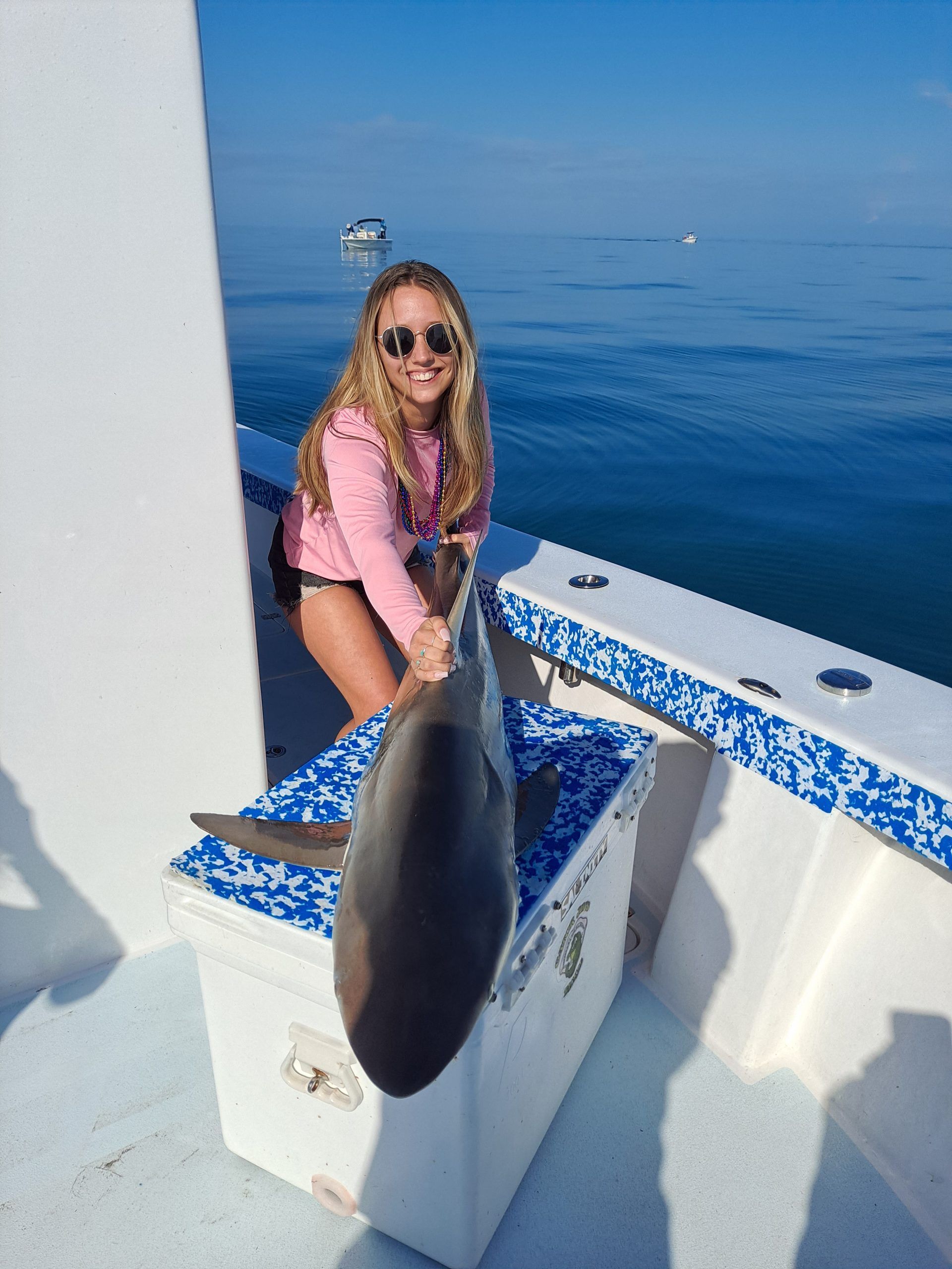 Woman on a boat holding a small shark. She's smiling. Ocean in background.