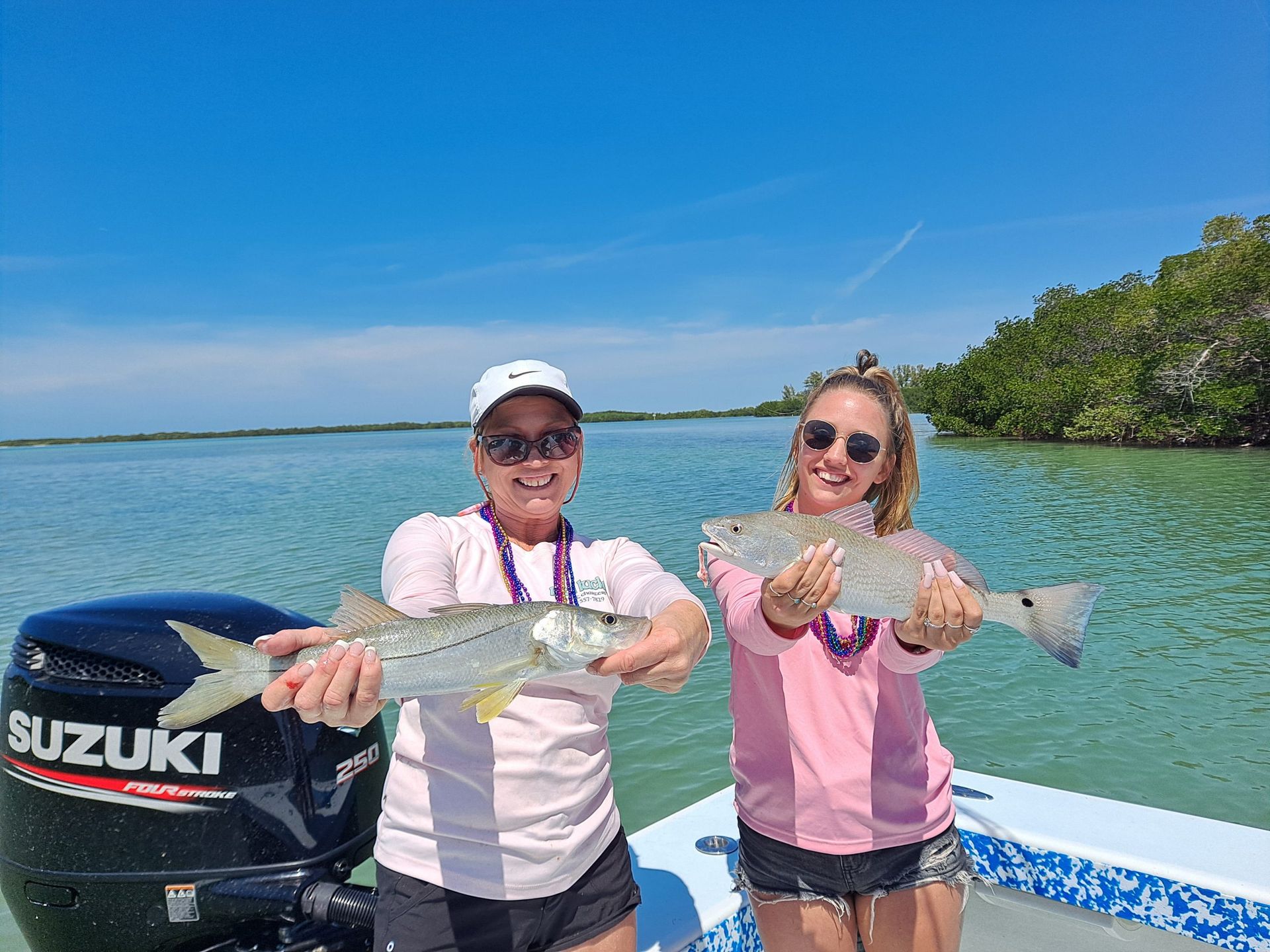 Two women on a boat holding up fish they caught, blue water, sunny day.