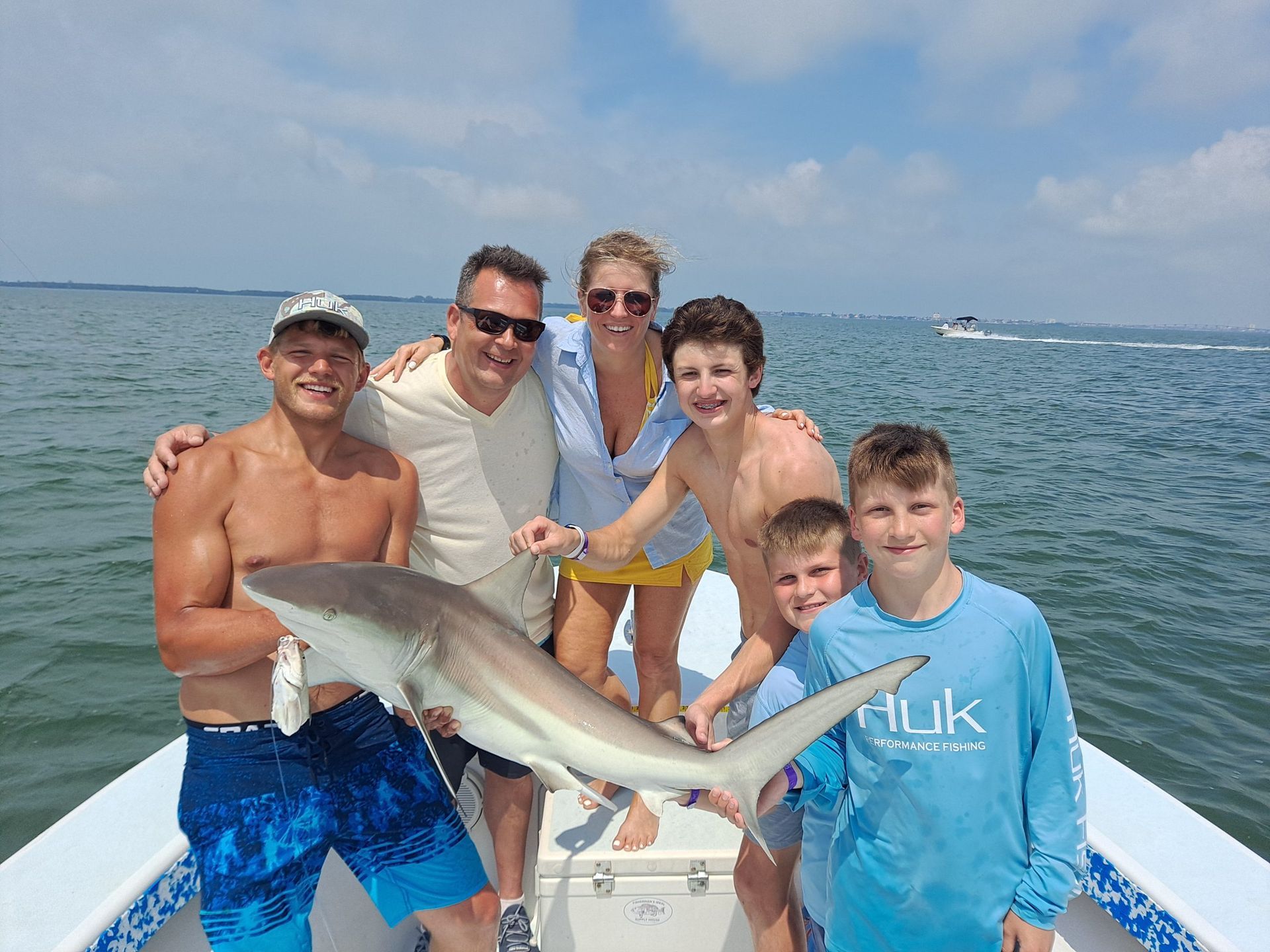 Family on a boat holding up a shark they caught; blue water and sky.