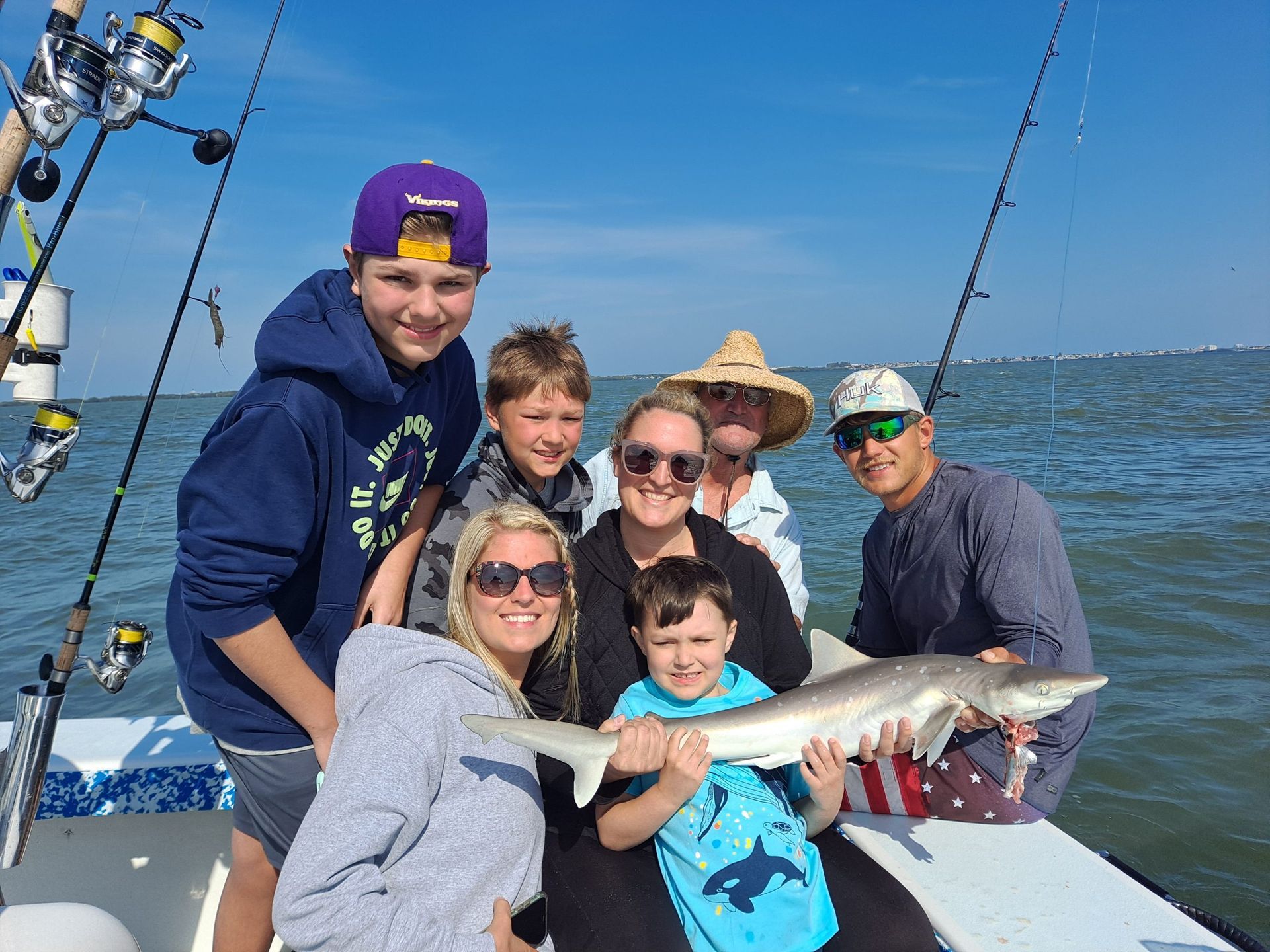 Family on a boat fishing, smiling with a caught shark on a sunny day.