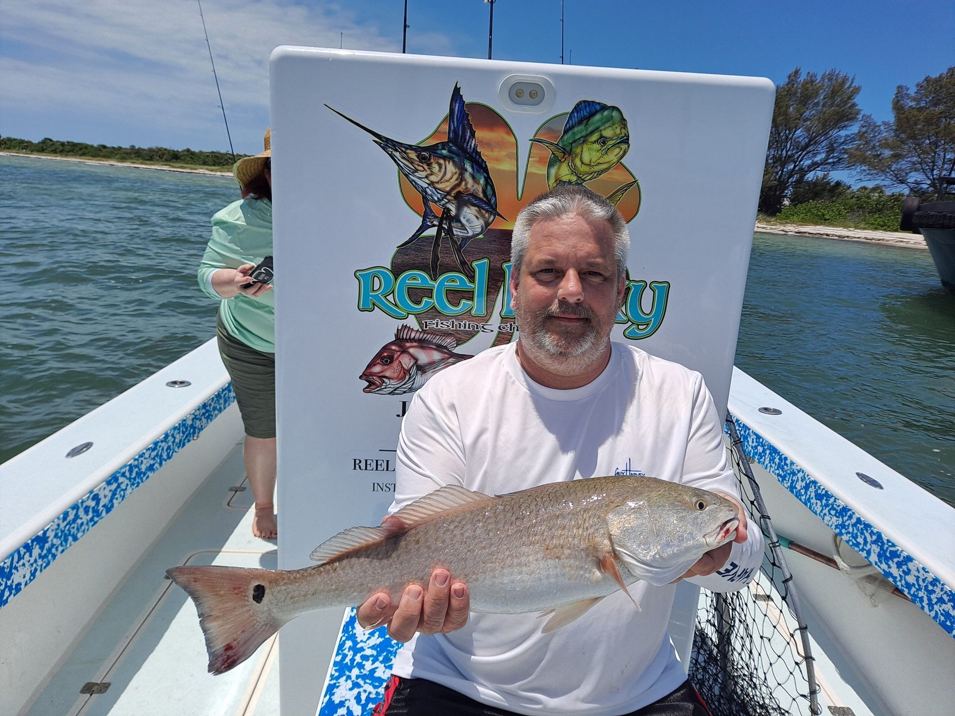 Man on boat holding a large redfish, smiling, with a 