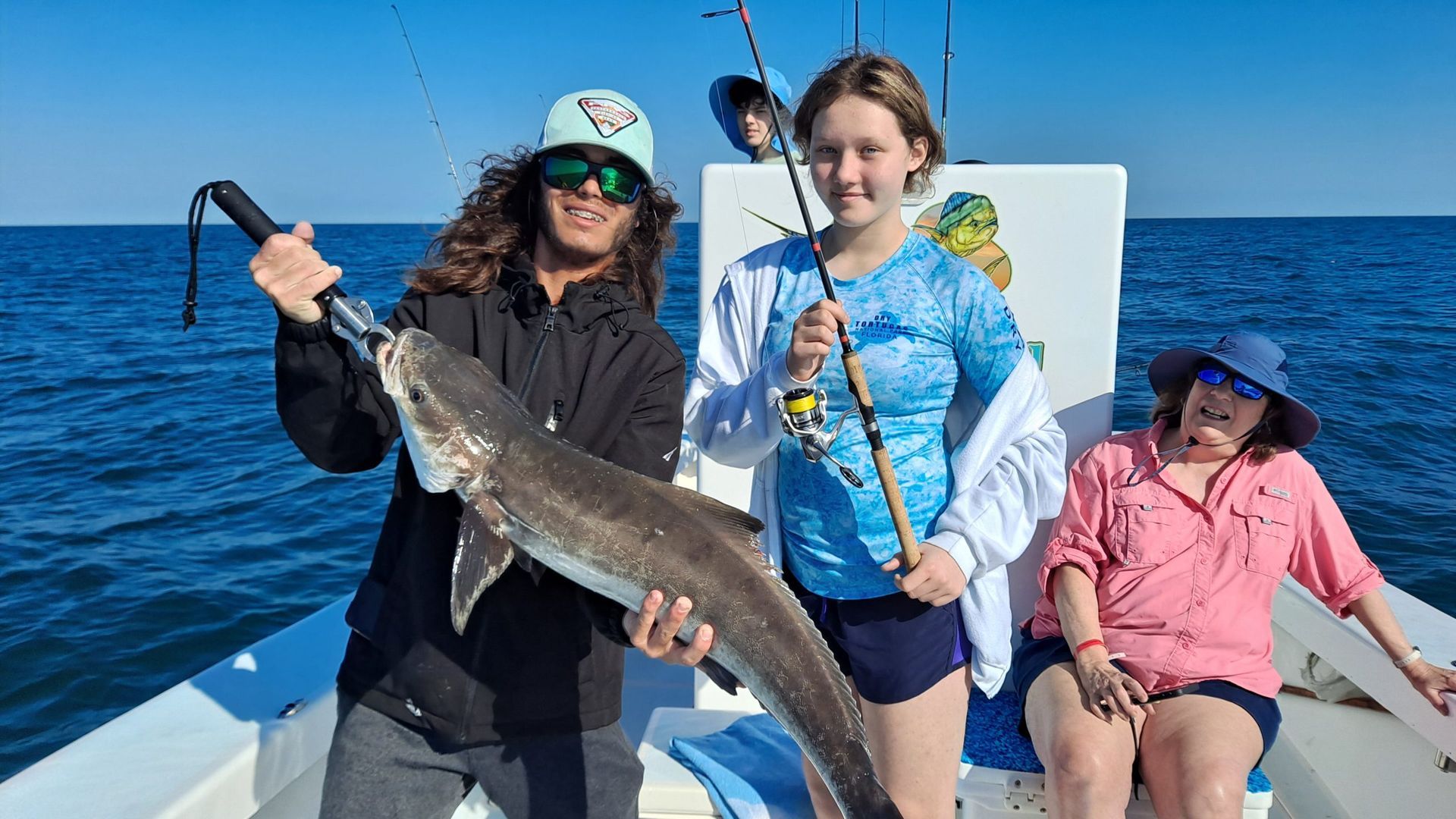 Three people on a boat with a caught fish in the ocean on a sunny day.