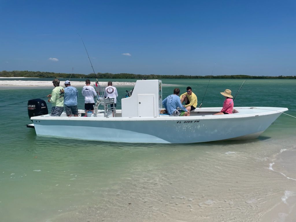 People fishing from a light blue boat near a sandy beach on a sunny day.