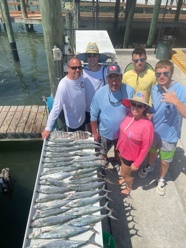 Group of people with a large haul of fish on a dock near a waterway on a sunny day.
