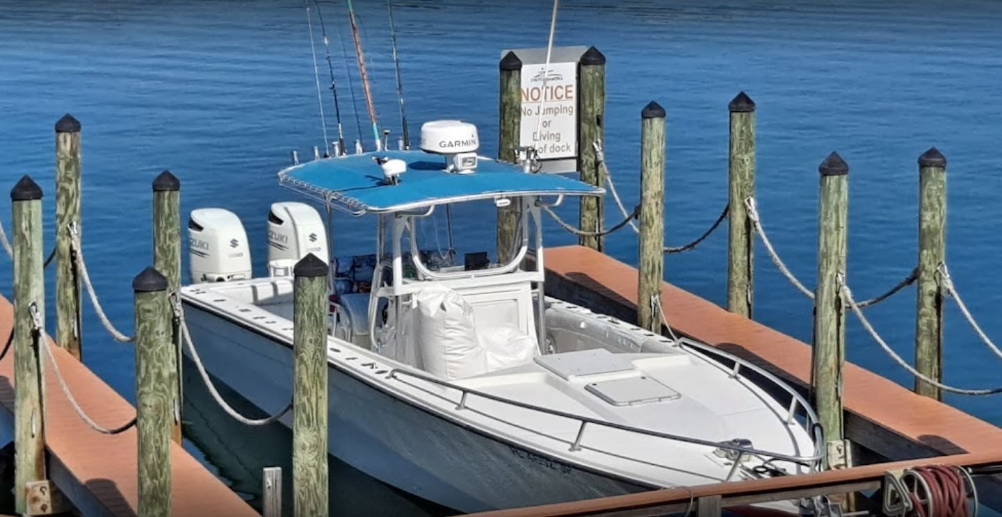 White boat docked, blue canopy, two outboard motors, at a pier with wooden posts, calm water.