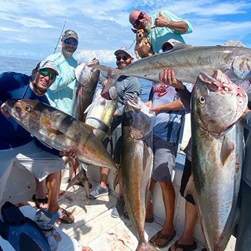 Group of people on a boat holding up fish they caught. Sunny day at sea.