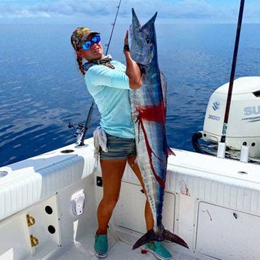 Woman on a boat holding a large, freshly caught wahoo fish. Blue ocean background.