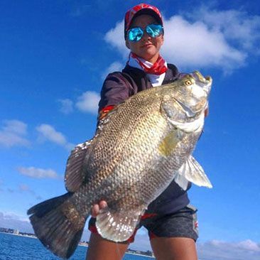 Woman holding a large black fish with blue sky background.