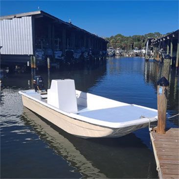 Small, tan boat docked near a wooden pier. Blue water and sunny day.