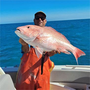 Man holding a large red snapper on a boat. Blue ocean, sunny day.