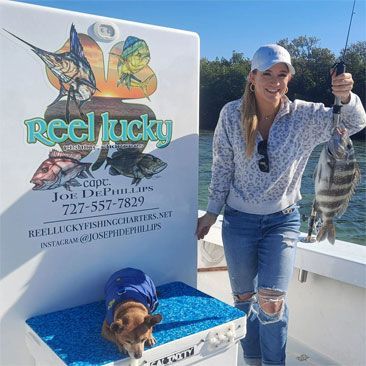 Woman on a boat holding a fish, a small dog wearing a jacket sits nearby.