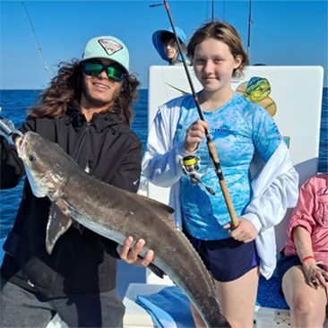 Man and girl on a boat hold a large fish they caught. Ocean background, blue sky, sunny day.