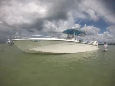 White boat beached in shallow water; person standing nearby under cloudy sky.