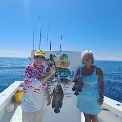 Two women on a boat holding fish, sunny day, blue ocean, sign for fishing charter.