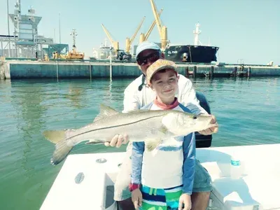 Boy holding a fish on a boat, with a man in the background. Port setting on a sunny day.
