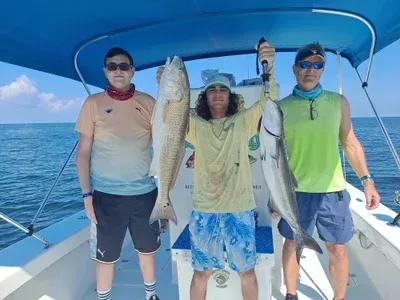 Three people on a boat holding up fish they caught; sunny day.