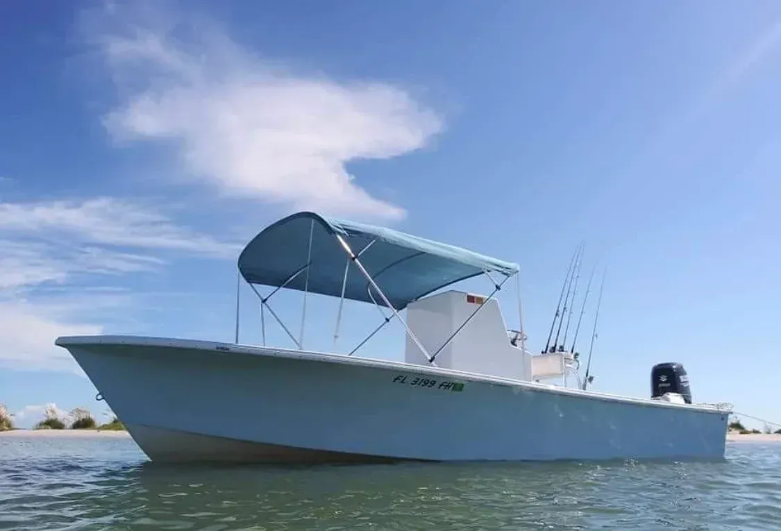 Light blue fishing boat with a blue canopy on calm water, against a bright blue sky.