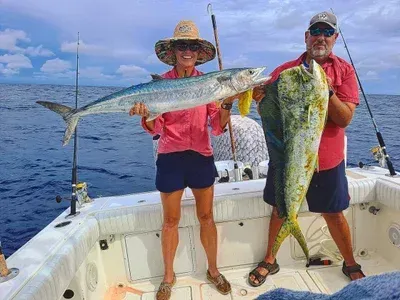 Two people on a boat holding up large fish they caught in the ocean.