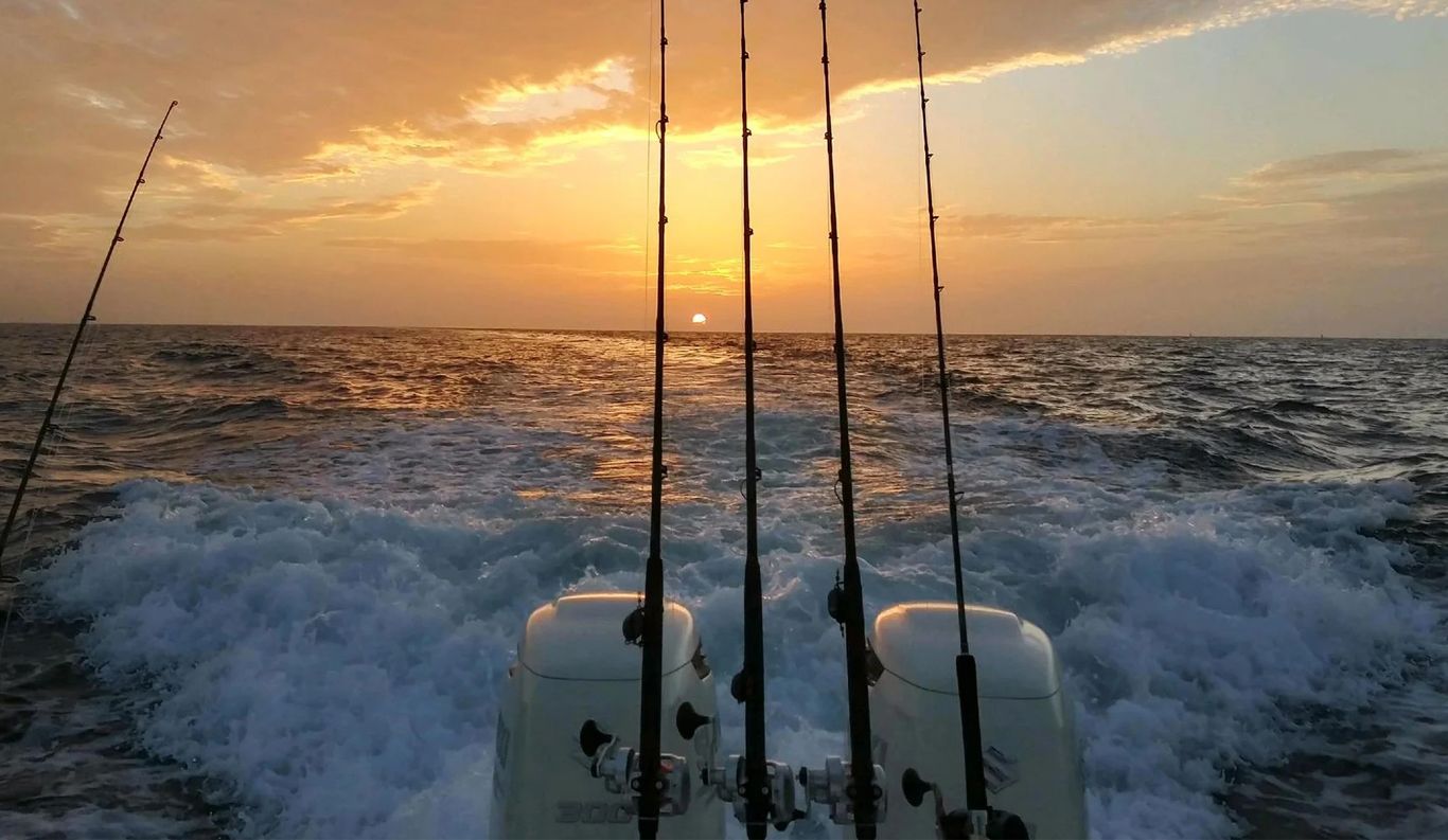 Fishing rods on a boat, silhouetted against a sunset over the ocean.
