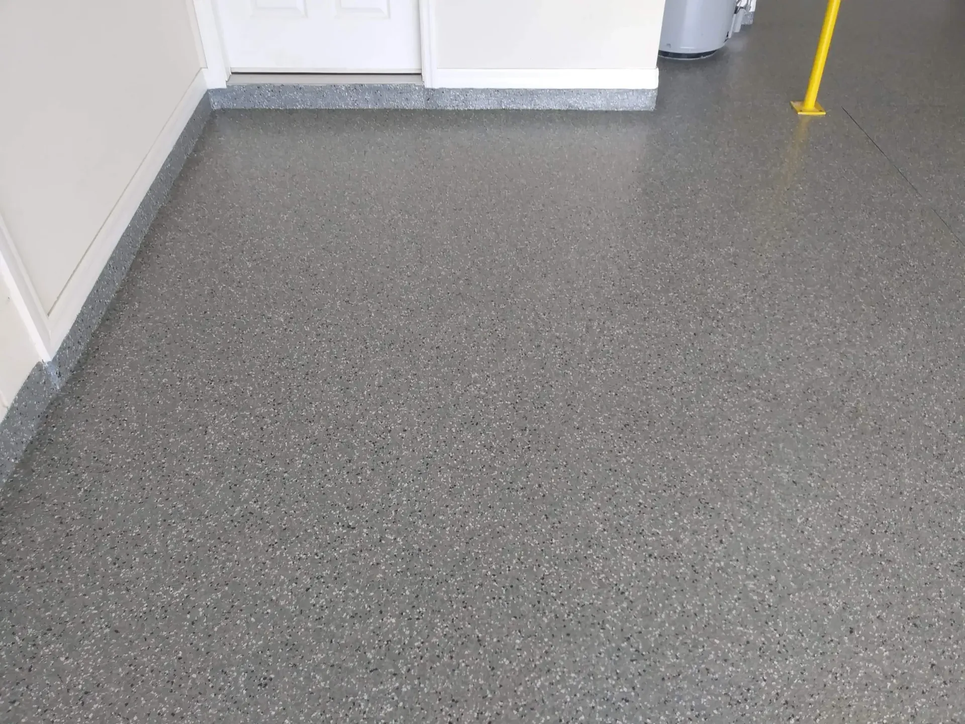 Gray speckled epoxy floor with white trim and door in a garage.