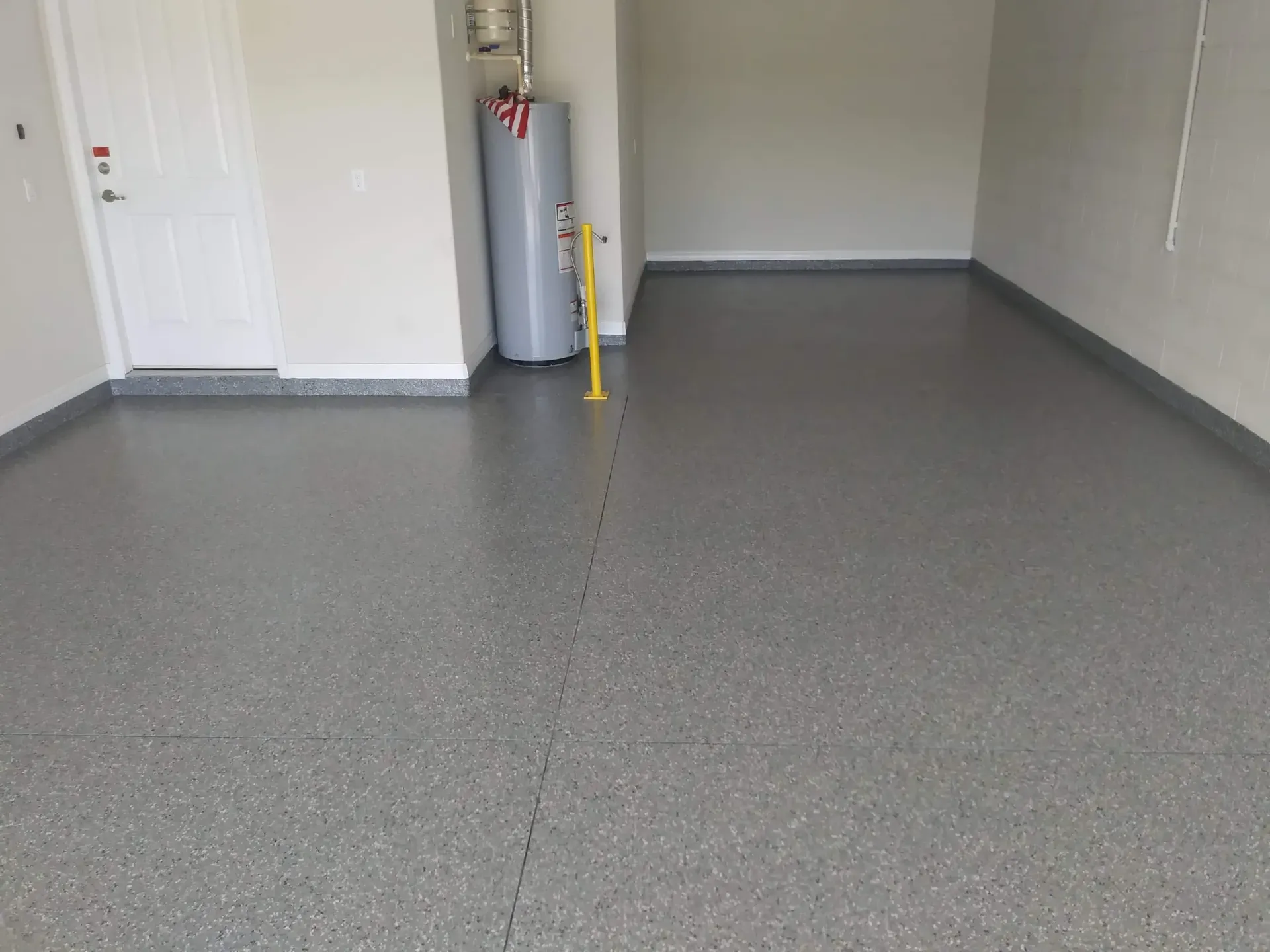 Garage with gray speckled epoxy floor, white walls, water heater, and a door.