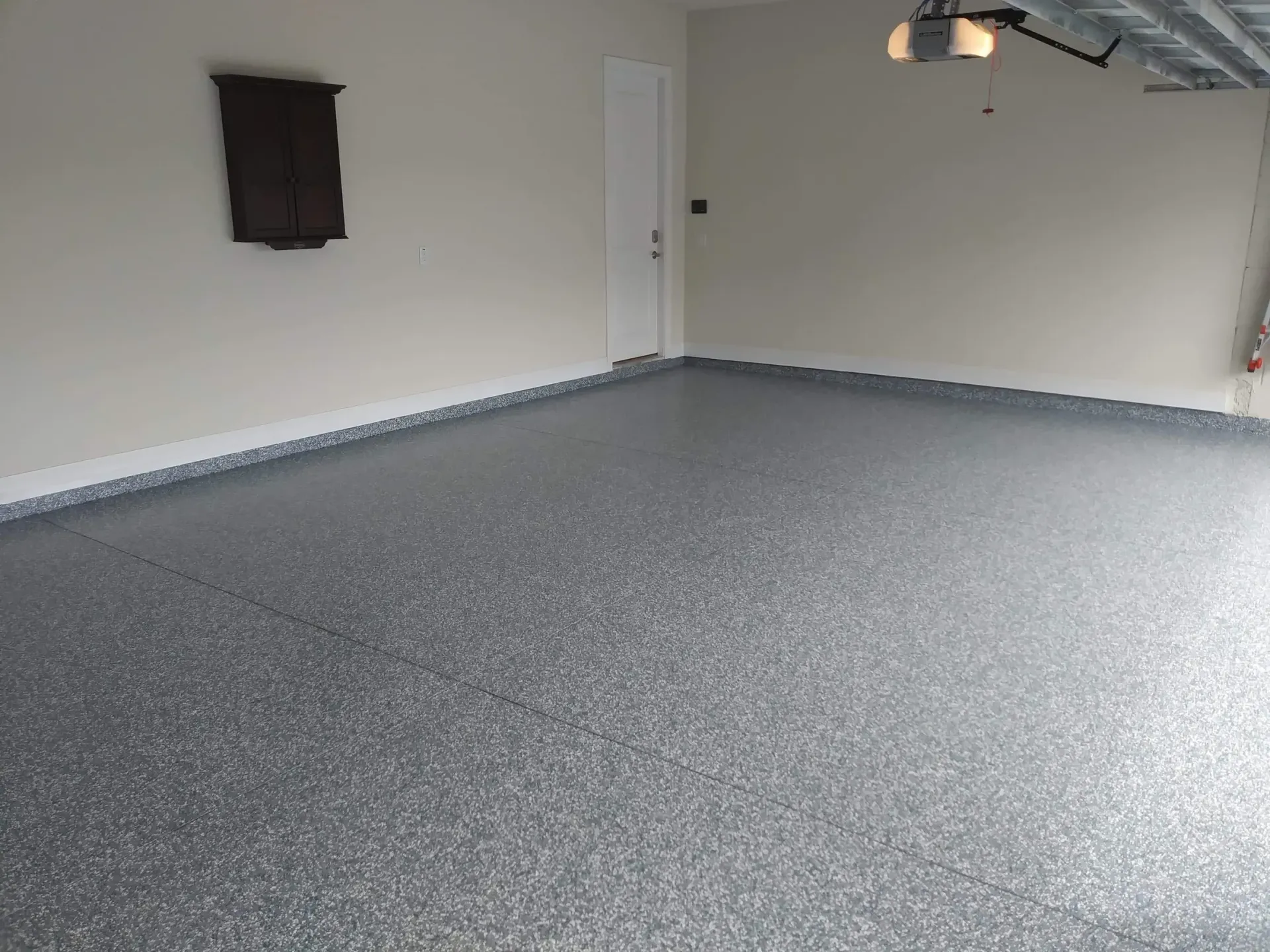 Gray speckled epoxy floor in a garage with light beige walls, a closed door, and a dark brown object.