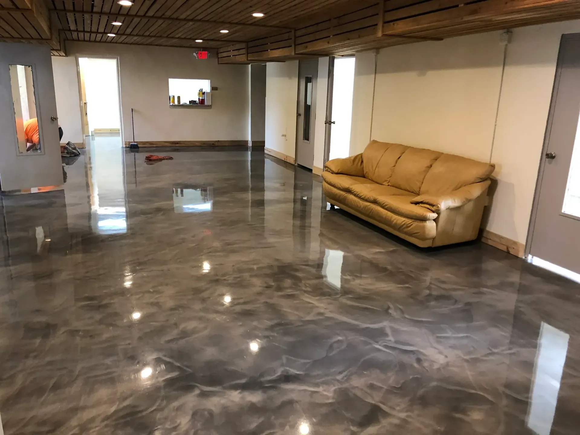 Gray epoxy floor in a large room, beige couch, white walls, doors.