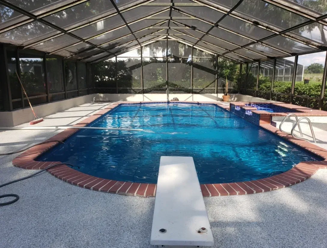 Indoor swimming pool with a diving board, surrounded by a screened enclosure, with a brick border.