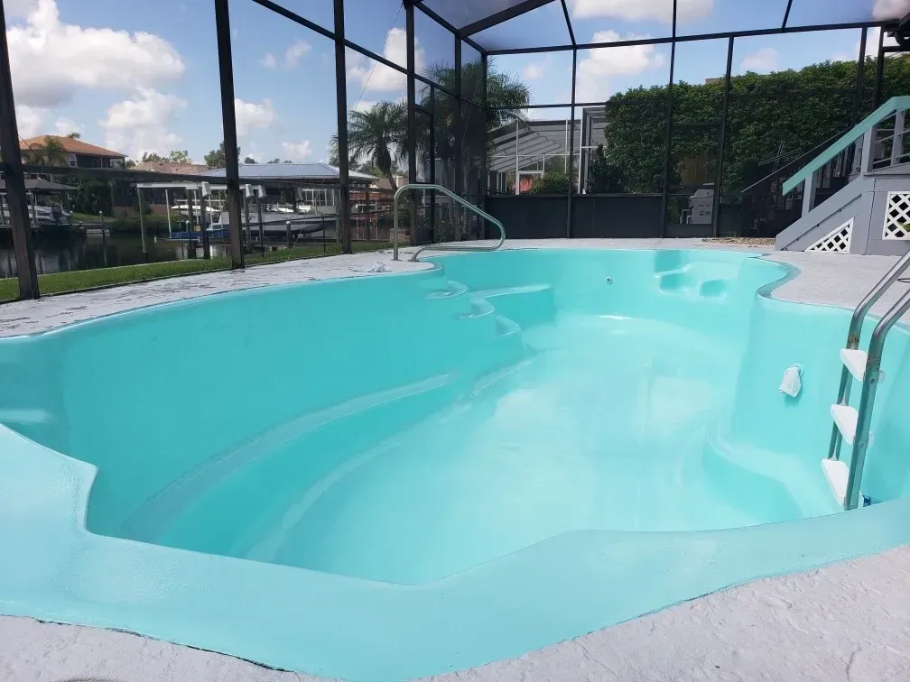Empty turquoise pool, part of a screened-in patio, overlooking a canal, on a sunny day.