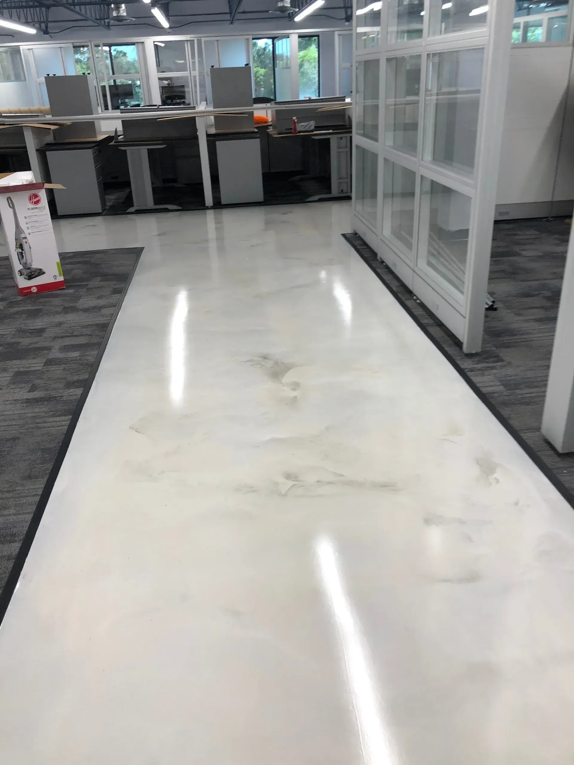 White epoxy floor in an office setting.  Dark smudges, gray carpet, glass partitions and desks in the background.