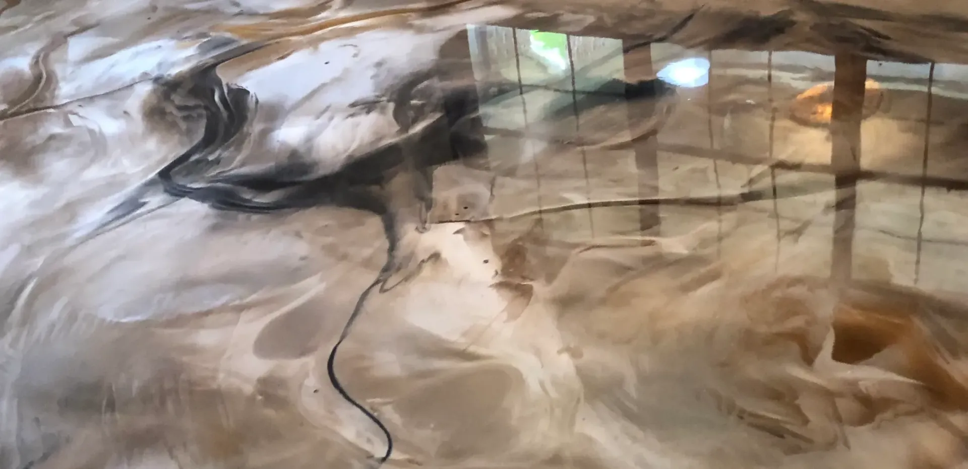 Swirled epoxy floor with shades of tan, black, and white, with window reflections.