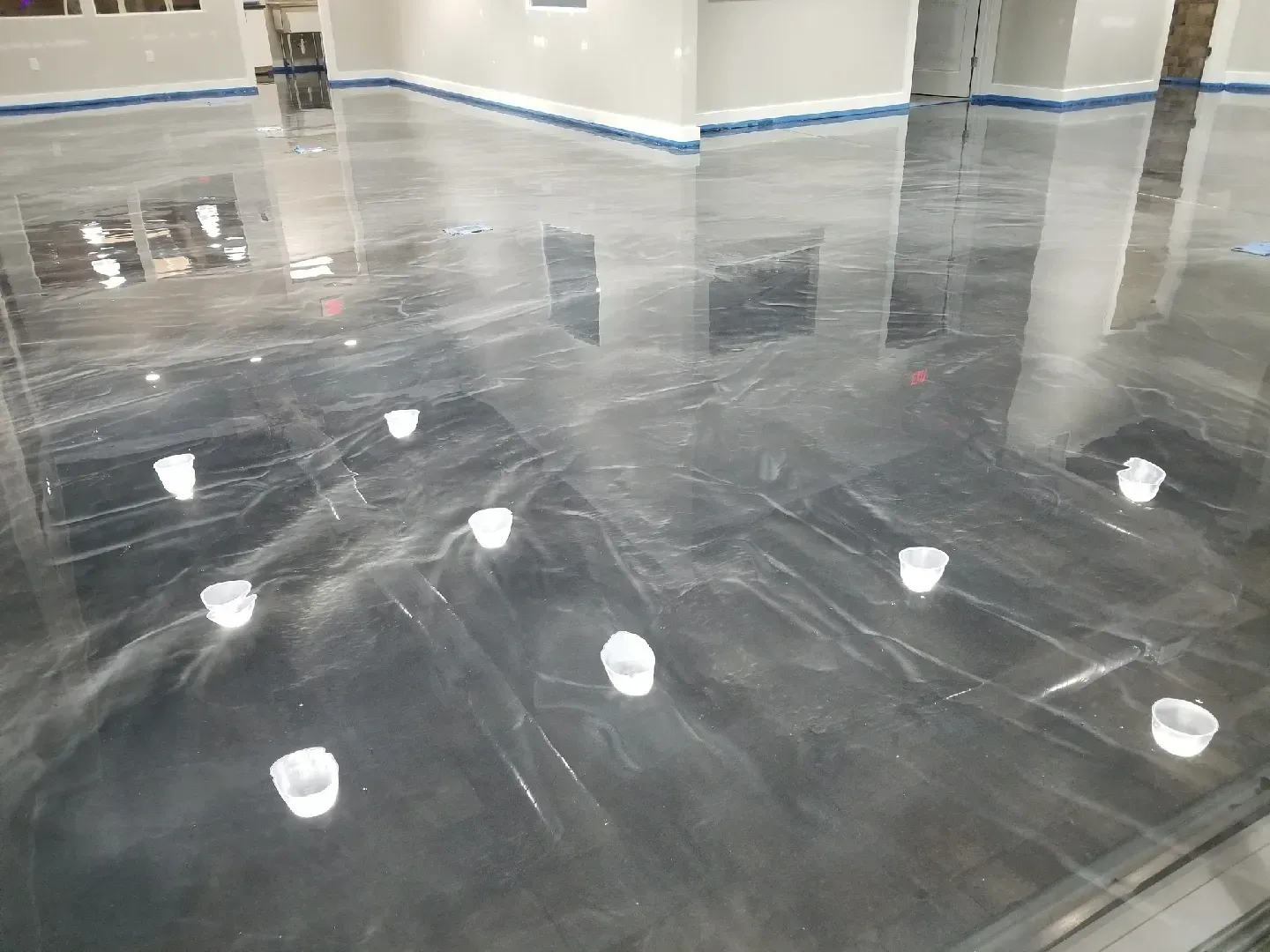 Shiny, metallic epoxy floor in a building. White cups are scattered on the surface.