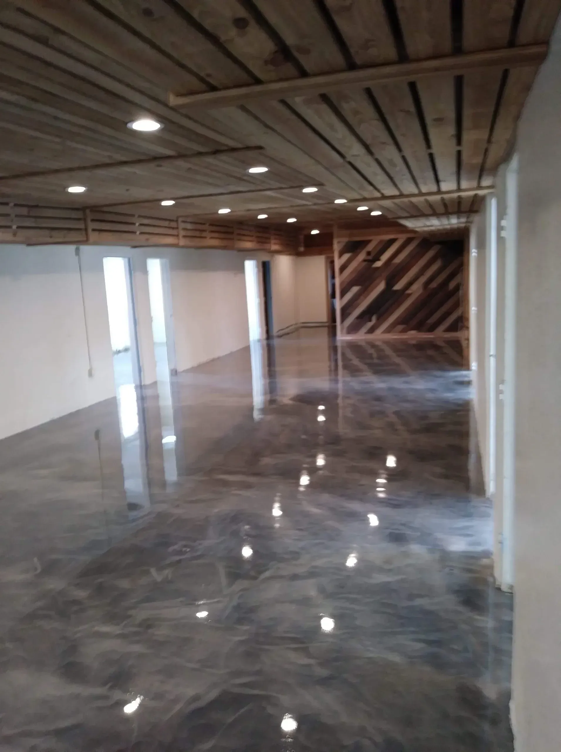 Empty commercial space with glossy, gray floor, wooden ceiling and accent wall.