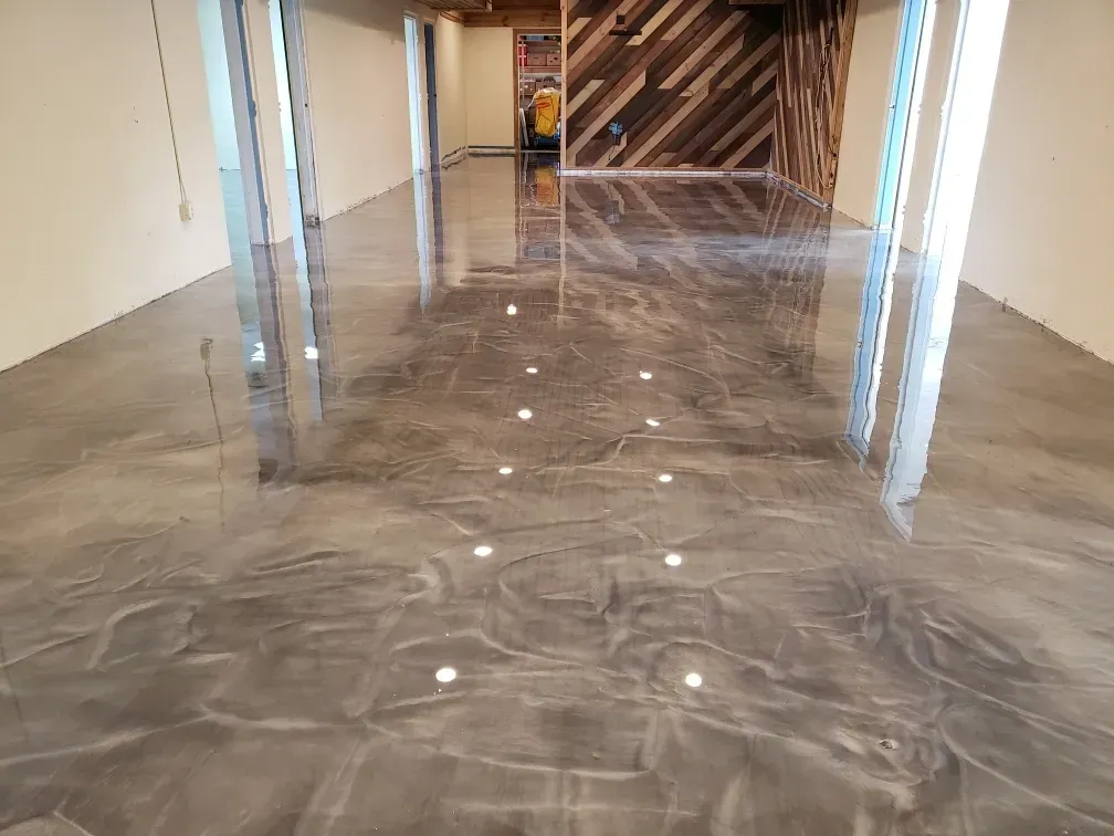 A room with a shiny, gray epoxy floor and recessed lights, with a wood accent wall in the back.