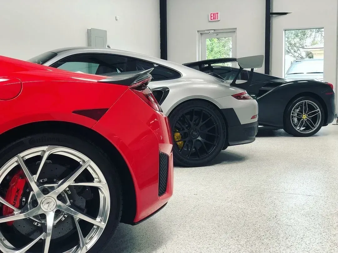 Red, silver, and black sports cars parked inside a garage with white walls and a light grey floor.