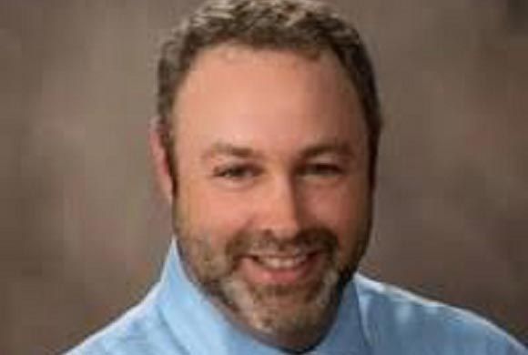 A man with a beard and a blue shirt is smiling for the camera.