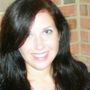 A woman with long black hair is smiling in front of a brick wall.