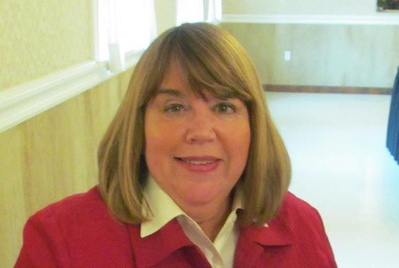 A woman in a red jacket and white shirt smiles for the camera