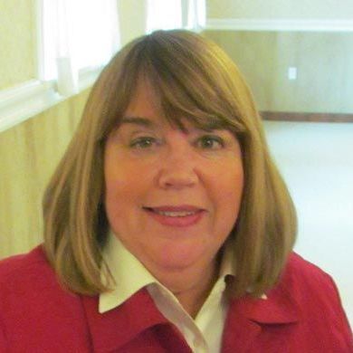A woman in a red jacket and white shirt is smiling for the camera.