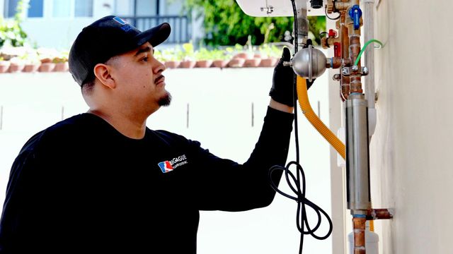 Technician inspecting outdoor plumbing pipes and valves beside a wall