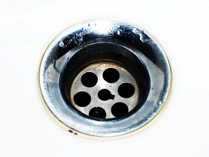 Close-up of a chrome sink drain with circular holes and dark water inside