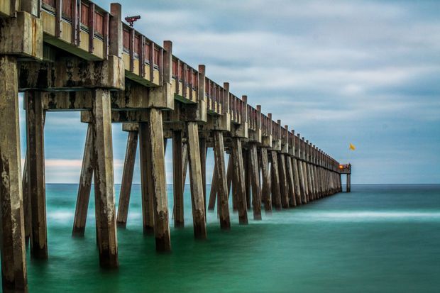 A long wooden pier leading into the ocean on a cloudy day.